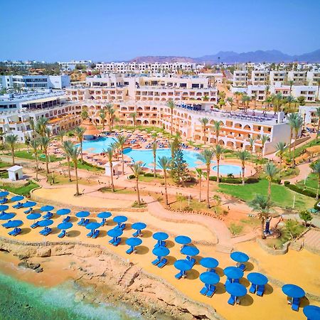 Pickalbatros Royal Grand Sharm - Adults Friendly 16 Years Plus Ngoại thất bức ảnh The photo shows a vibrant resort area with several buildings that appear to be accommodations or hotel units. There are multiple swimming pools surrounded by palm trees, creating a tropical atmosphere. In the foreground, there is a beach area with sa