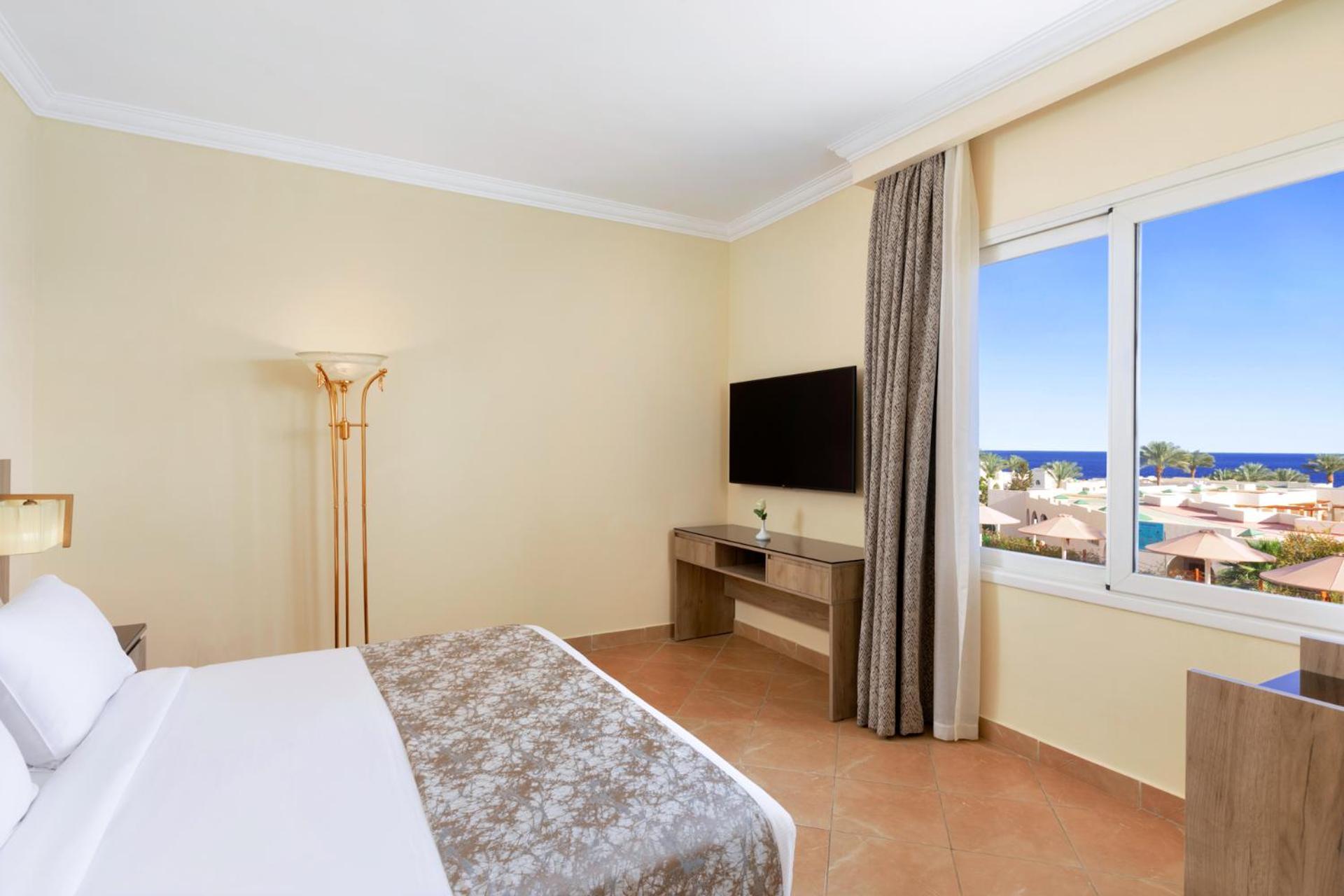 Pickalbatros Royal Grand Sharm - Adults Friendly 16 Years Plus Ngoại thất bức ảnh The photo shows a hotel room with a modern and minimalistic design. There is a comfortable bed with white linens and a decorative gray throw at the foot. A large window offers a view of the outdoors, possibly with a glimpse of the sea or beach. A fla