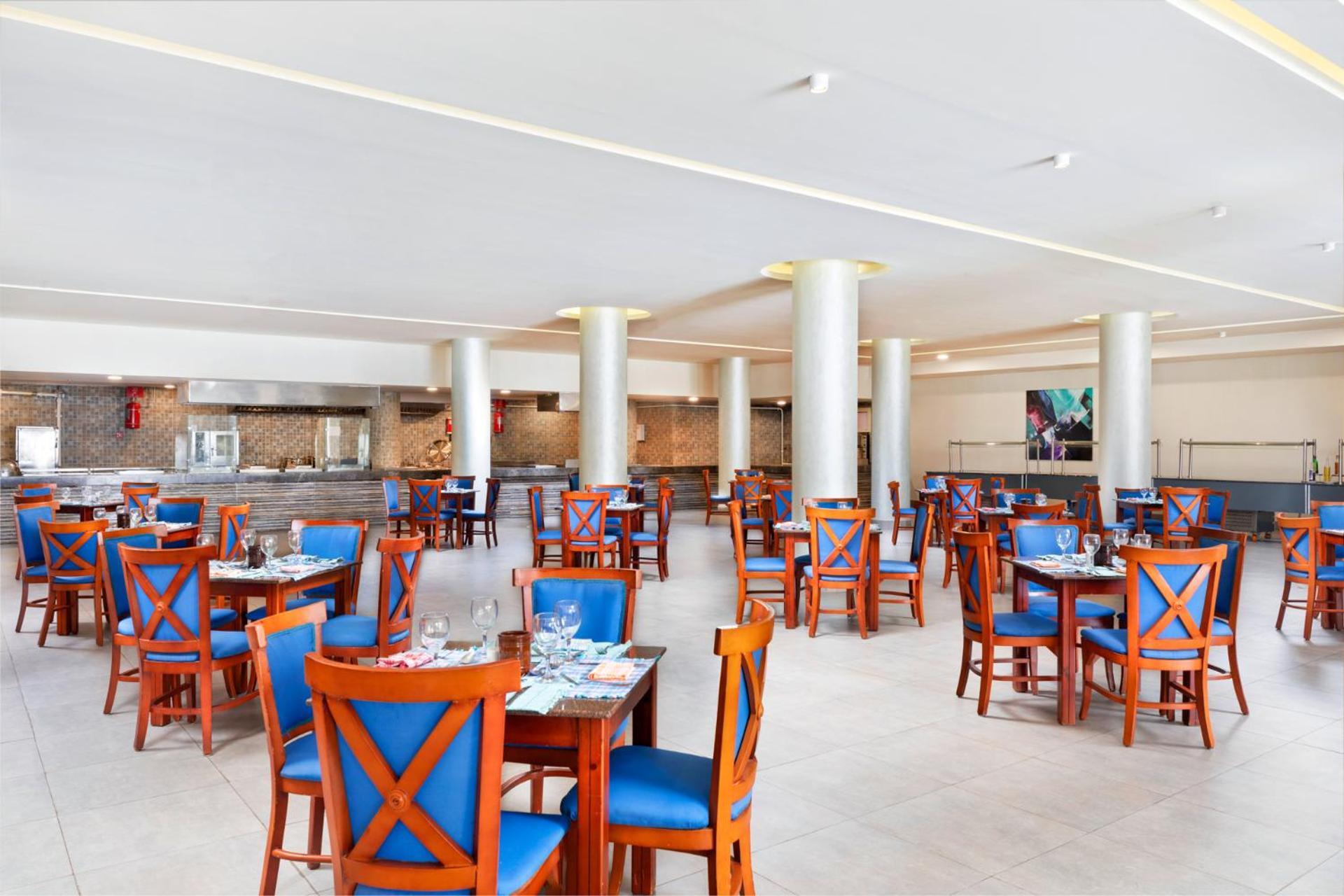 Pickalbatros Royal Grand Sharm - Adults Friendly 16 Years Plus Ngoại thất bức ảnh The photo depicts a spacious dining area in a restaurant. The room features several wooden tables, each with blue chairs. The chairs have a unique design with prominent X-shaped backs. The flooring is light-colored tile, and the walls are painted in 