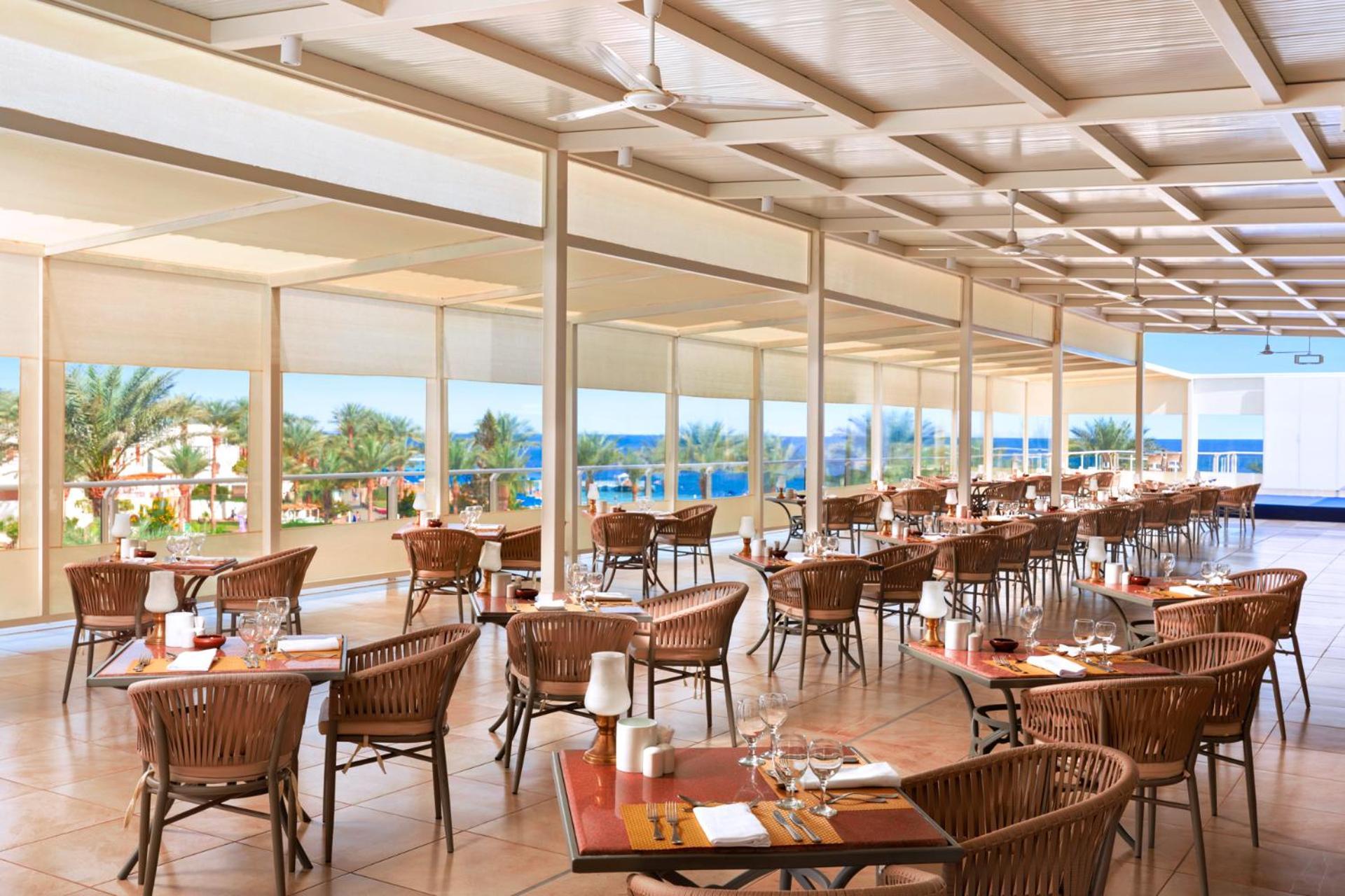 Pickalbatros Royal Grand Sharm - Adults Friendly 16 Years Plus Ngoại thất bức ảnh The photo shows a spacious dining area in a restaurant with a modern and airy design. It features numerous wooden tables set with glasses and cutlery, arranged in a way that gives an open feel. Large windows provide a view of the outside, showcasing 