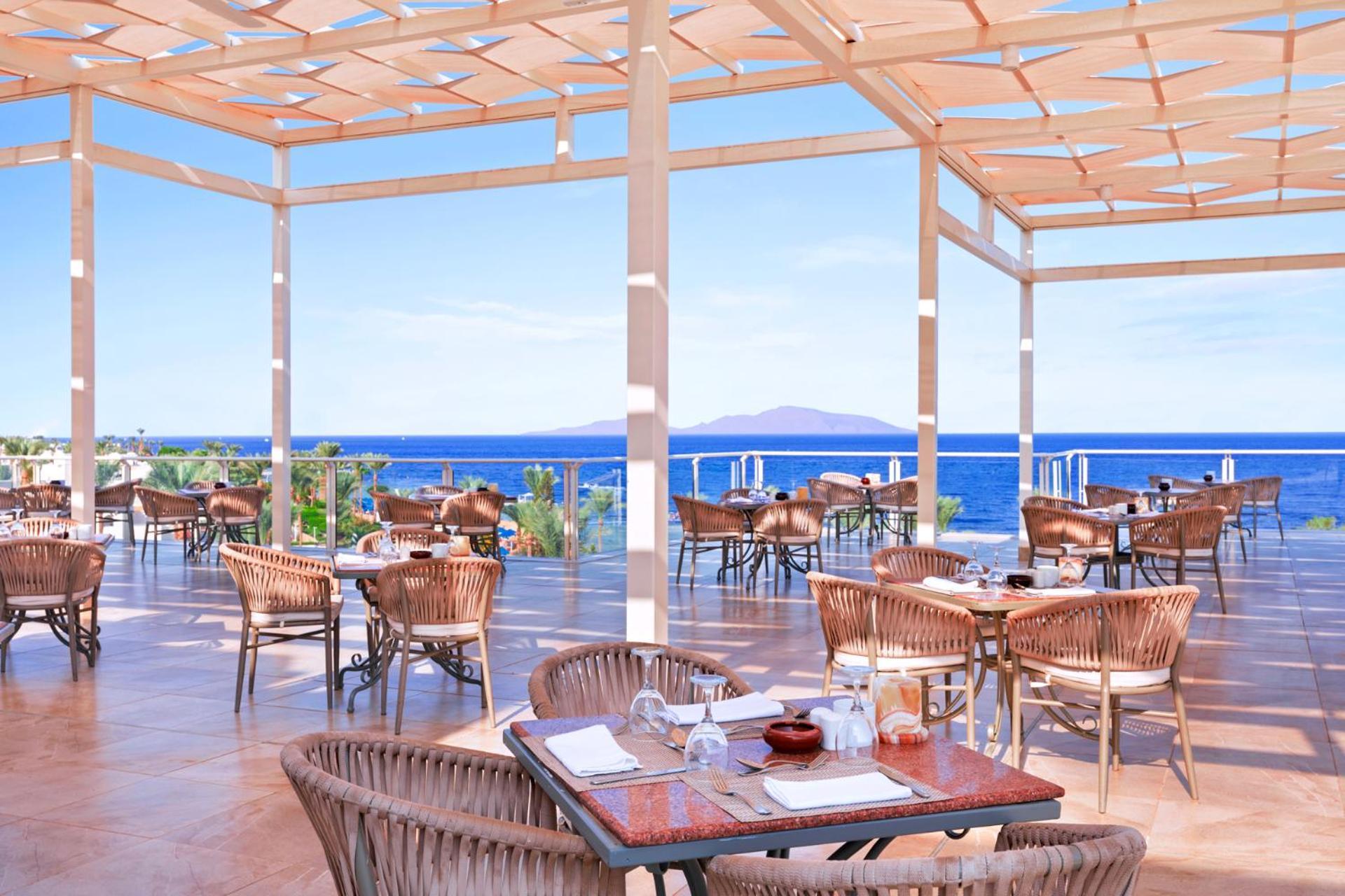Pickalbatros Royal Grand Sharm - Adults Friendly 16 Years Plus Ngoại thất bức ảnh The photo shows a spacious outdoor restaurant with a beautiful view of the ocean. The seating area features several tables and wicker chairs. The open design includes a wooden pergola providing some shade, while large windows or openings allow for a 