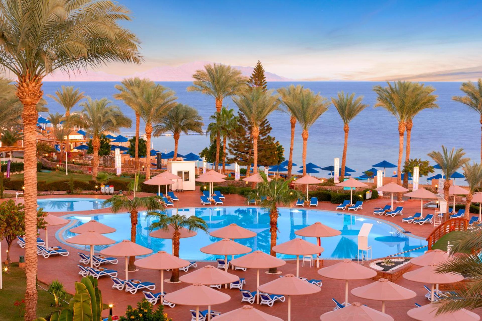 Pickalbatros Royal Grand Sharm - Adults Friendly 16 Years Plus Ngoại thất bức ảnh The photo shows a beautiful resort scene with a swimming pool surrounded by lounge chairs and umbrellas. Palm trees line the area, adding to the tropical atmosphere. In the background, there is a view of the sea under a clear sky, suggesting a peacef