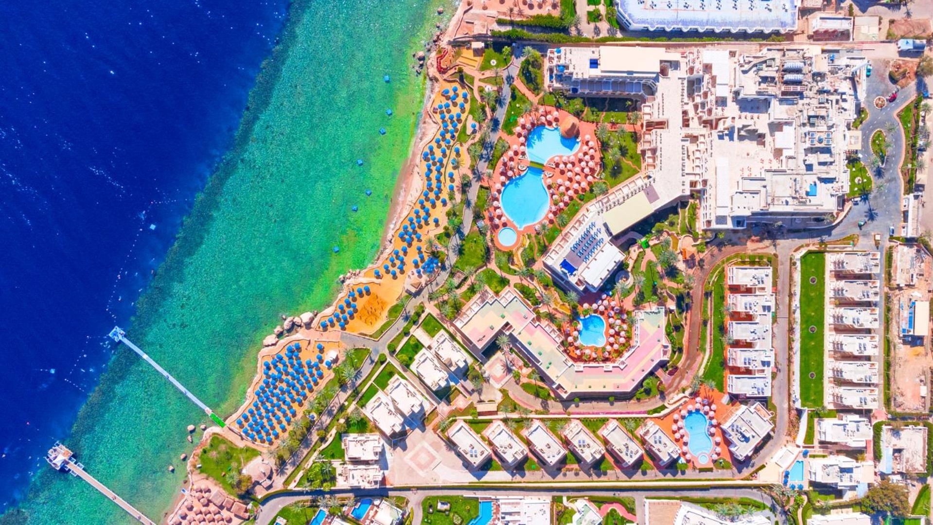 Pickalbatros Royal Grand Sharm - Adults Friendly 16 Years Plus Ngoại thất bức ảnh The image shows an aerial view of a coastal resort area. It features various swimming pools outlined by landscaped gardens and pathways. There are also rows of sun loungers and umbrellas near the beach. The water transitions from a deep blue to a vib