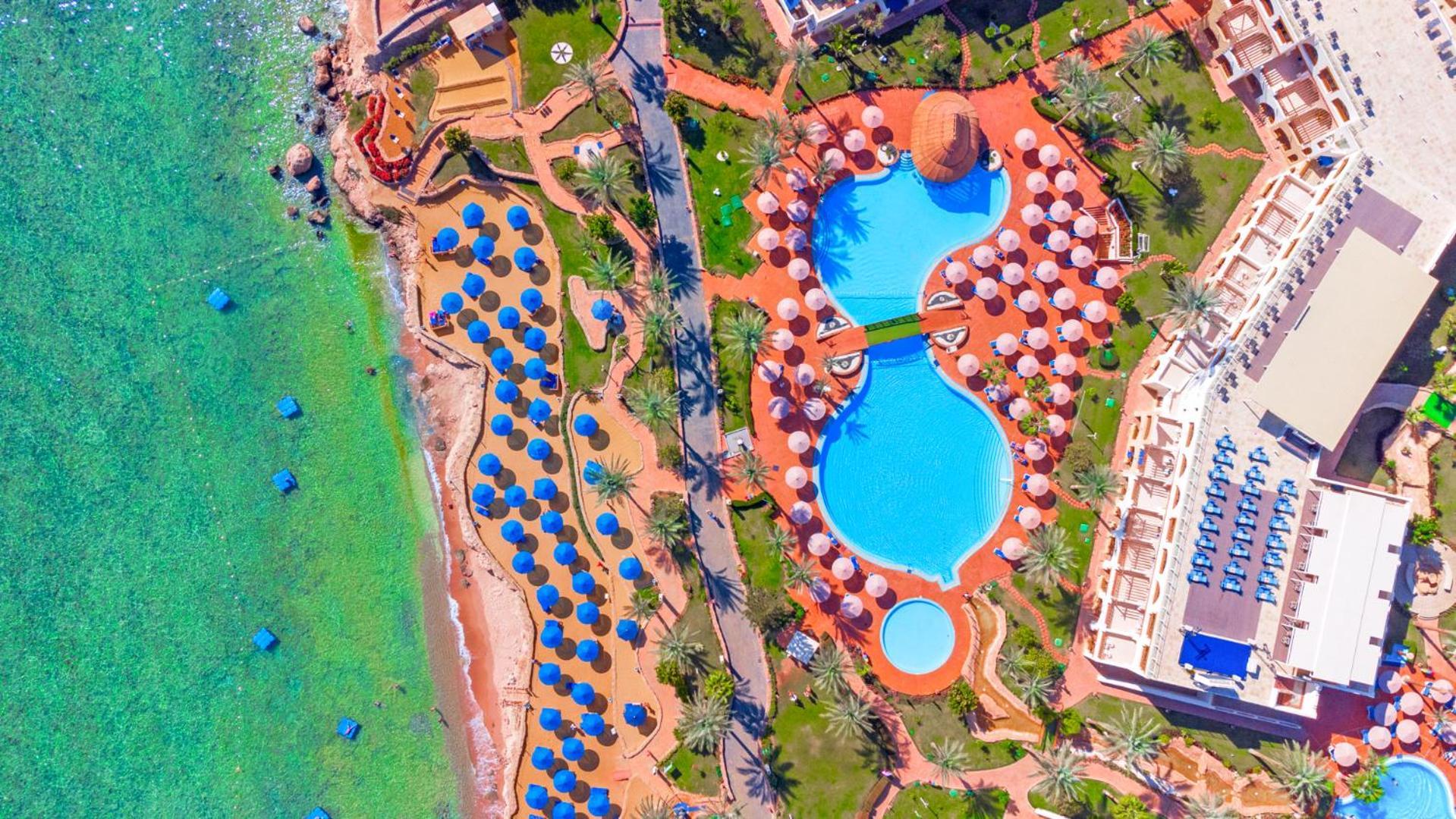 Pickalbatros Royal Grand Sharm - Adults Friendly 16 Years Plus Ngoại thất bức ảnh The photo shows an aerial view of a beach resort. In the foreground, there's a large swimming pool shaped like a flowing river, surrounded by lounge chairs and umbrellas. The pool has a distinctive, organic design with curved edges. To the left, ther