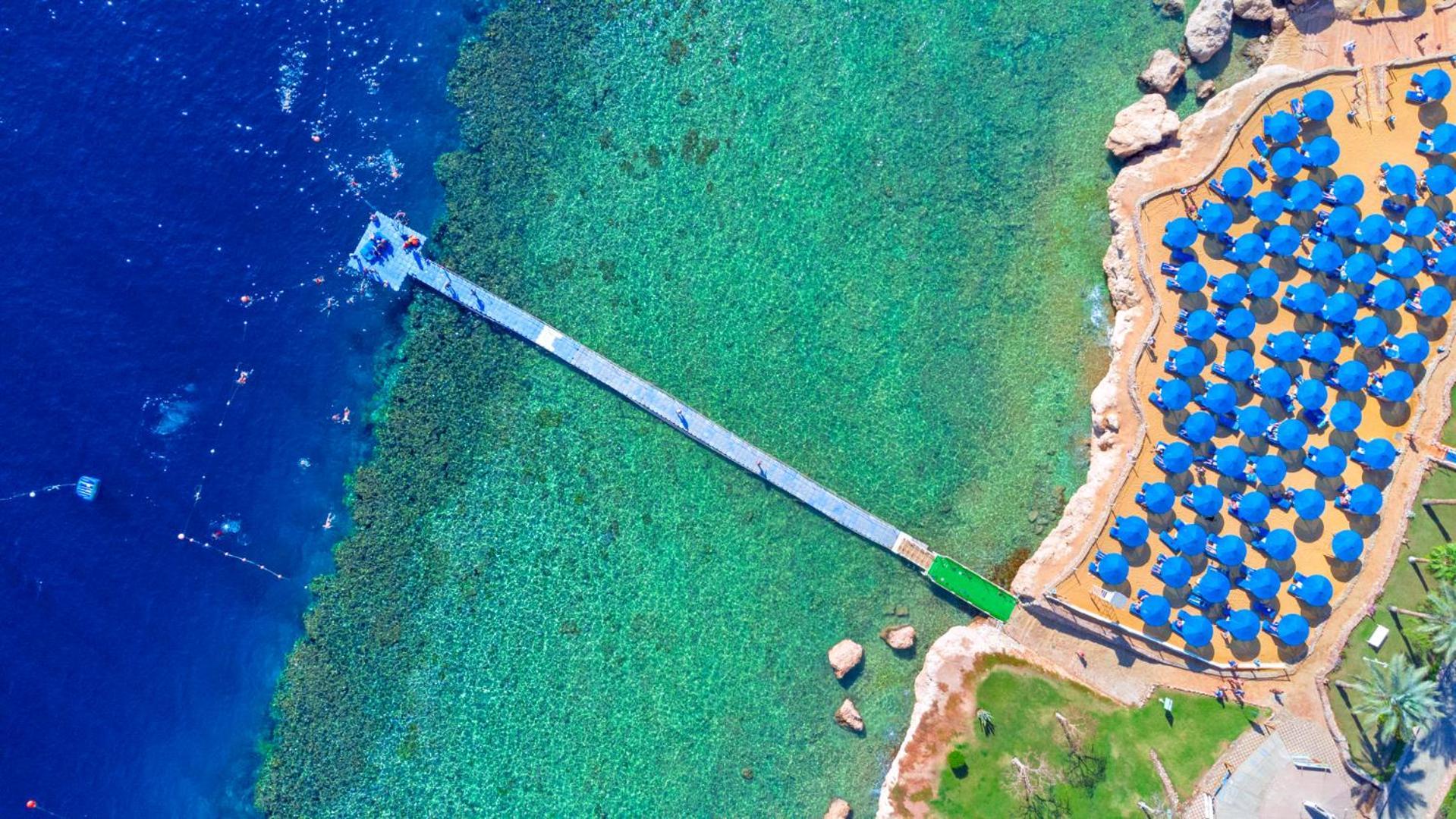 Pickalbatros Royal Grand Sharm - Adults Friendly 16 Years Plus Ngoại thất bức ảnh The photo shows an aerial view of a coastal area featuring a long wooden pier extending into clear turquoise water. On one side of the pier, there appears to be a beach with umbrellas or sunbeds arranged neatly. The water is vibrant and visually invi