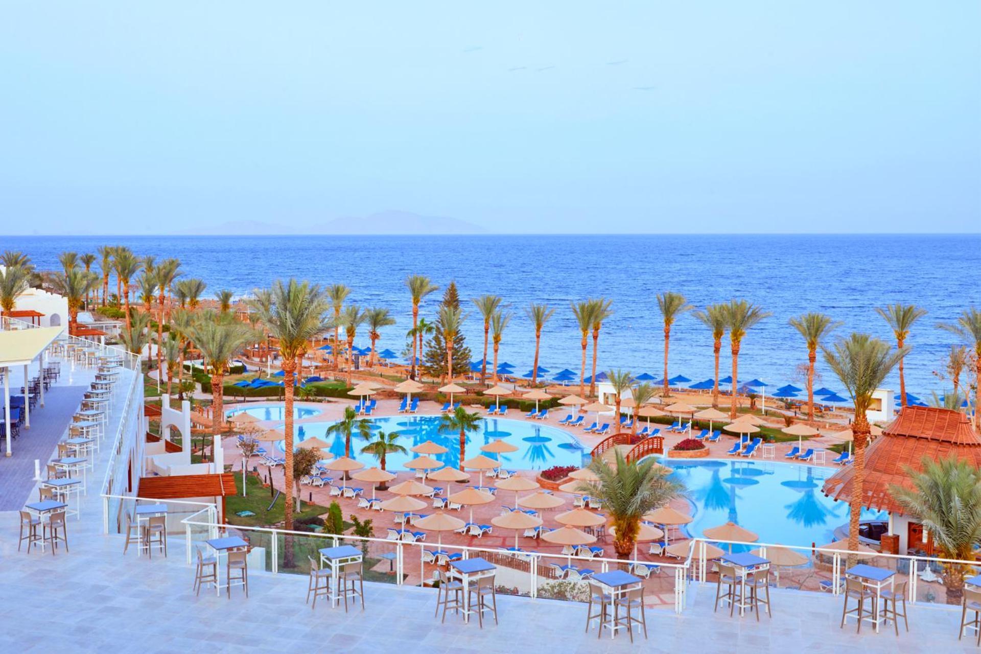 Pickalbatros Royal Grand Sharm - Adults Friendly 16 Years Plus Ngoại thất bức ảnh The photo depicts a scenic resort area by the sea. In the foreground, there is a large swimming pool surrounded by lounge chairs and umbrellas. Palm trees line the sides of the pool, adding to the tropical atmosphere. In the background, a beautiful b