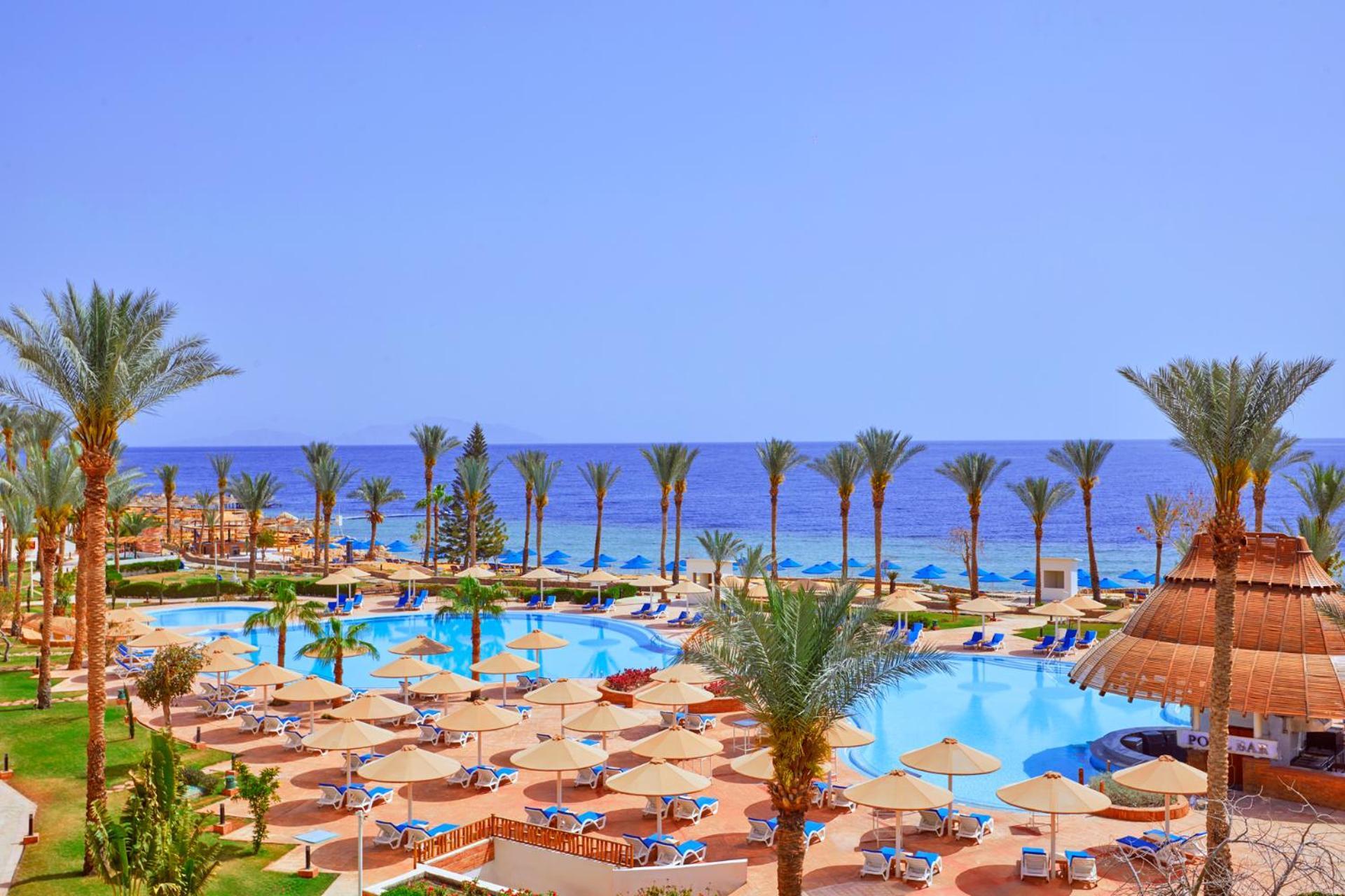 Pickalbatros Royal Grand Sharm - Adults Friendly 16 Years Plus Ngoại thất bức ảnh The photo showcases a beautiful resort setting by the sea. It features a large swimming pool surrounded by sunny lounge chairs and umbrellas, perfect for relaxation. The area is adorned with lush palm trees, adding to the tropical vibe. In the backgr