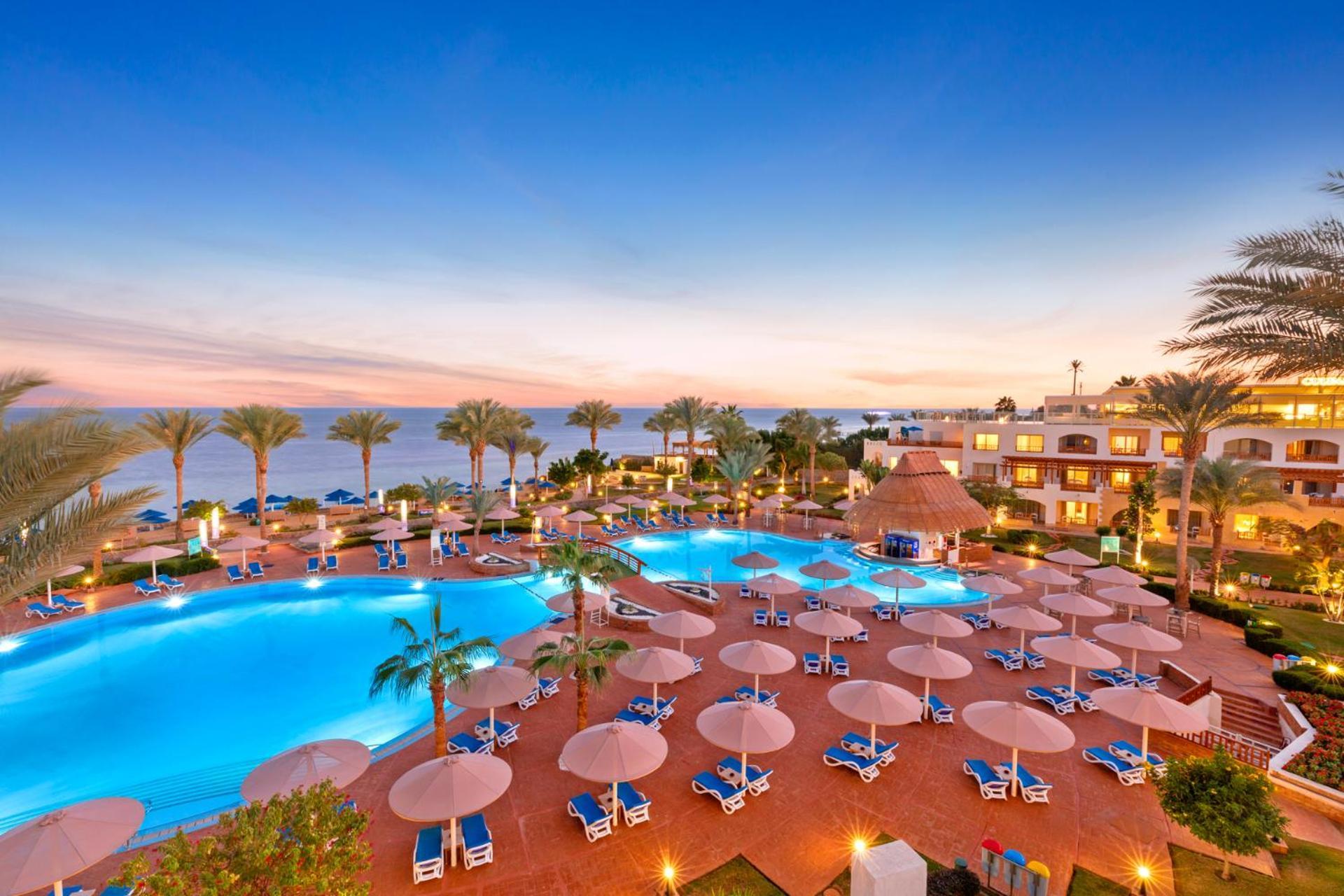 Pickalbatros Royal Grand Sharm - Adults Friendly 16 Years Plus Ngoại thất bức ảnh The photo showcases a luxurious resort setting with two large swimming pools, surrounded by lounge chairs and umbrellas. Palm trees are interspersed around the pool area, enhancing the tropical feel. In the background, there’s a view of the ocean, an