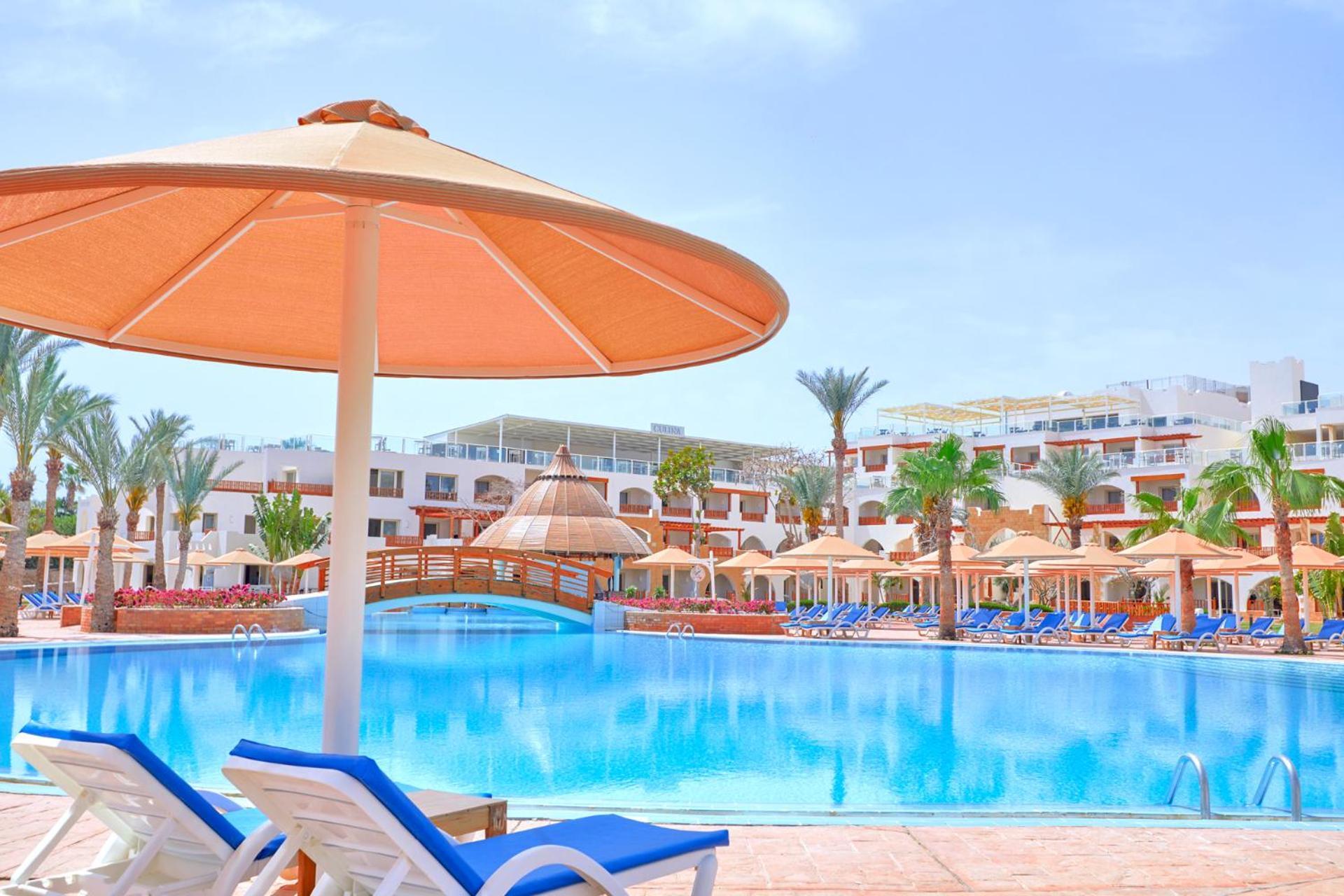 Pickalbatros Royal Grand Sharm - Adults Friendly 16 Years Plus Ngoại thất bức ảnh The photo shows a picturesque resort scene featuring a large swimming pool surrounded by lounge chairs and umbrellas. The pool is shimmering under a bright blue sky, and there are several palm trees in the background, adding to the tropical atmospher