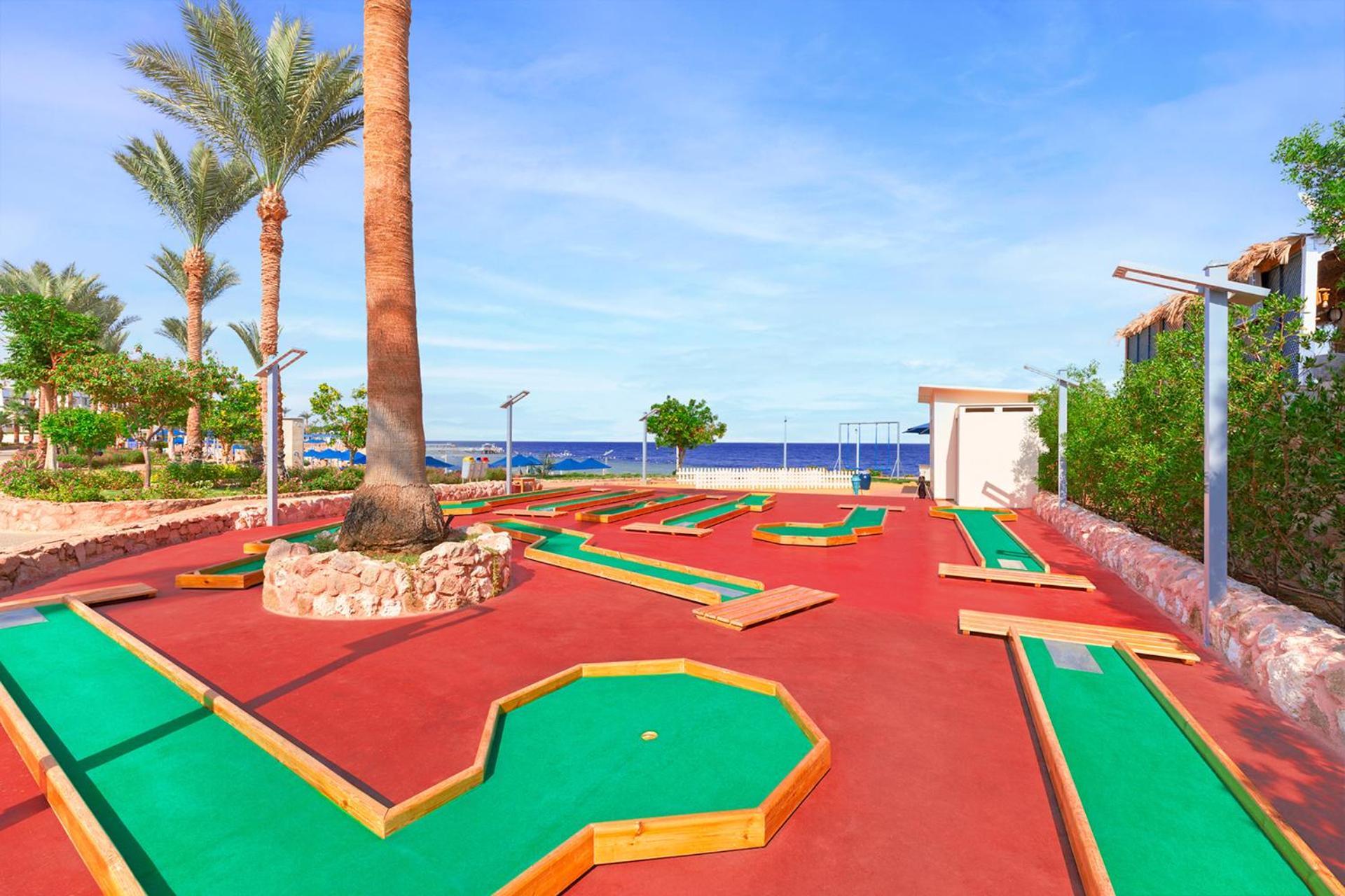 Pickalbatros Royal Grand Sharm - Adults Friendly 16 Years Plus Ngoại thất bức ảnh The photo shows a mini-golf course situated outdoors, with a view of the sea in the background. The course features vibrant green and red surfaces, laid out in winding patterns, and surrounded by well-maintained landscaping, including palm trees. The