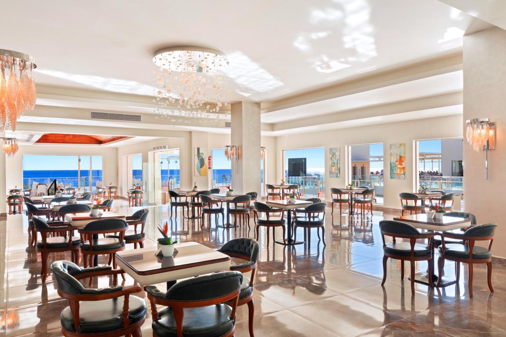 Pickalbatros Royal Grand Sharm - Adults Friendly 16 Years Plus Ngoại thất bức ảnh The photo shows a bright and elegant restaurant interior. There are several tables arranged throughout the space, each with chairs around them. The decor features modern lighting, including a chandelier, and large windows that allow natural light to 